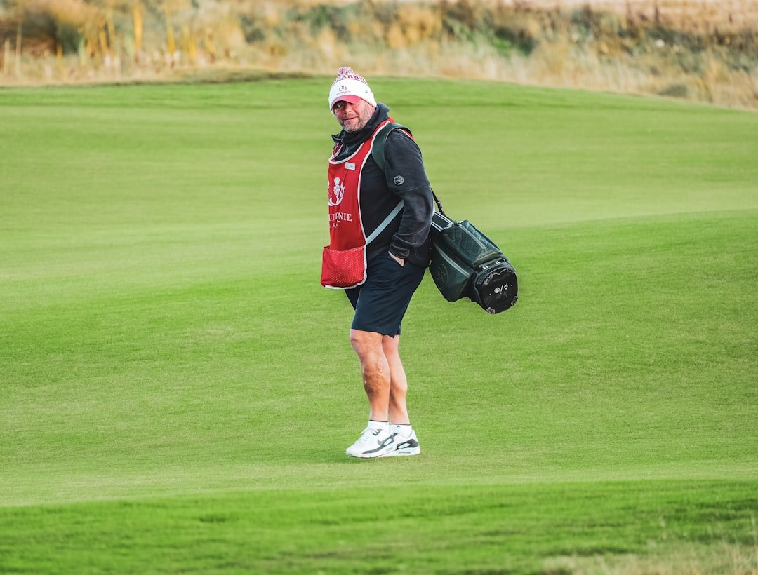 Golfer in layered cold-weather gear walking across a green course.