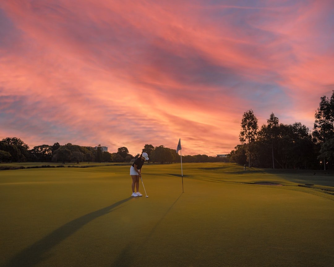 Golfer putting on a green beneath a dramatic sunset sky.