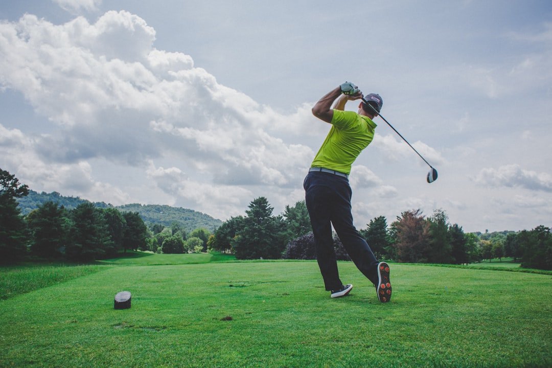 Golfer finishing a tee shot on an open fairway under a cloudy sky.